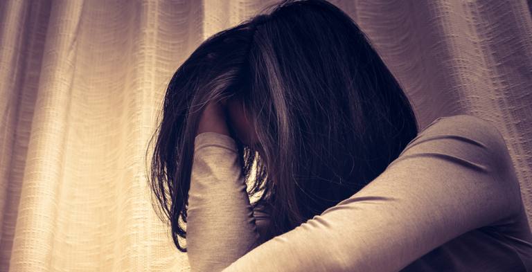 Woman with her head bowed and face buried in her arm