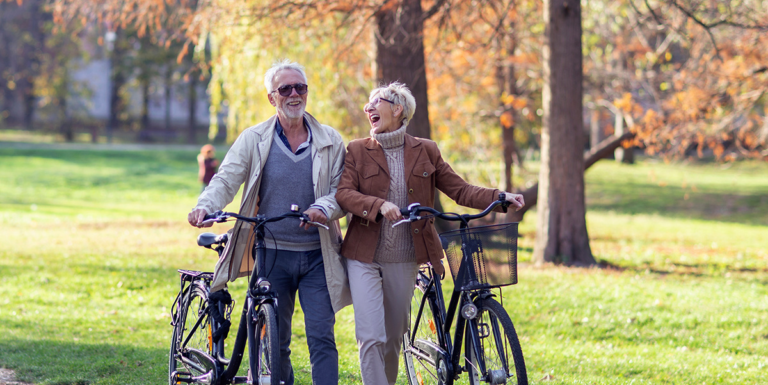 Man and woman laughing while walking bicycles through a park in autumn