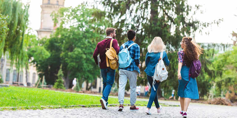 Four students with backpacks walking together on a campus path