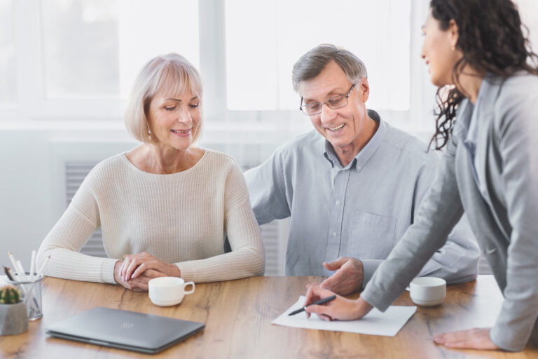 Man and woman seated at a table while another woman points to a document