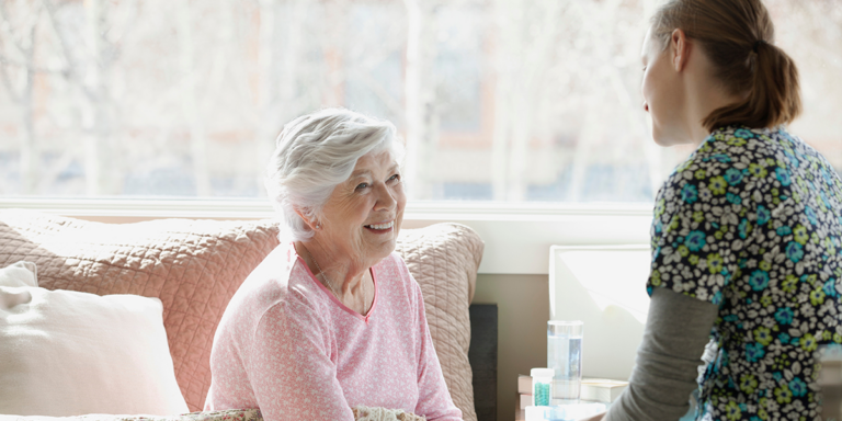 Older woman in bed talking with a nurse beside a glass of water and medication