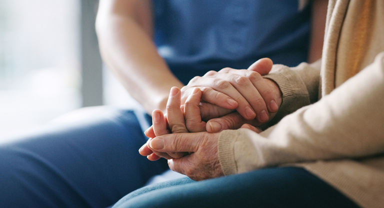 Person in scrubs holding an elderly person's hands