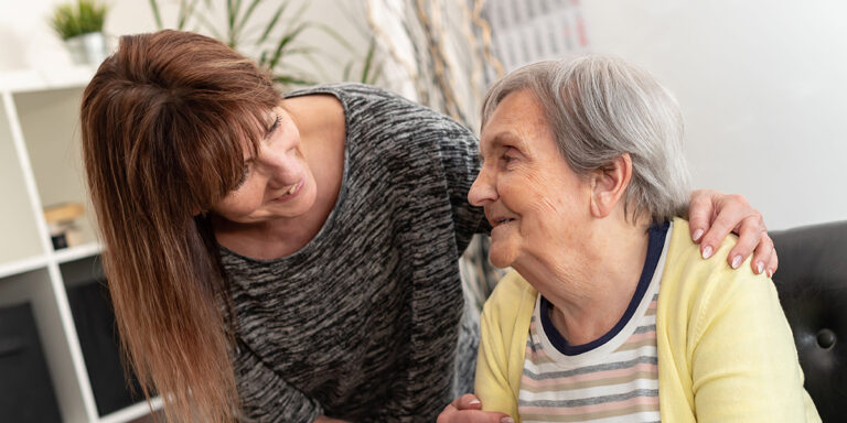 Woman smiling with her hand on an elderly woman's shoulder