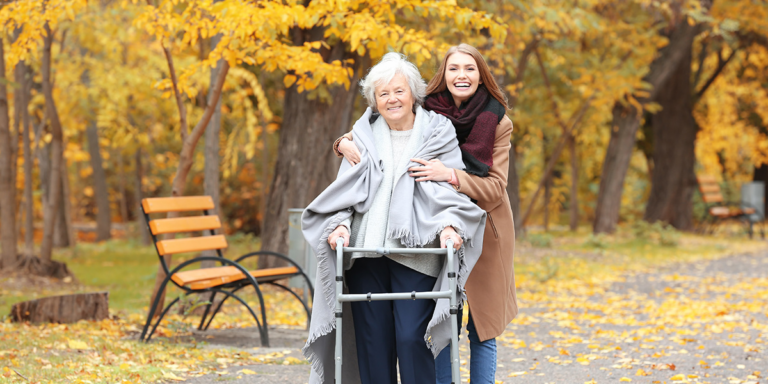 Older woman using a walker with a young woman beside her in a park