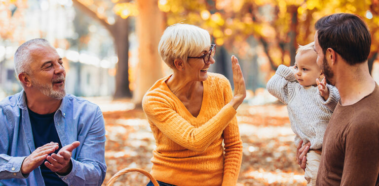 Man and woman talking with another man holding a baby outdoors in autumn