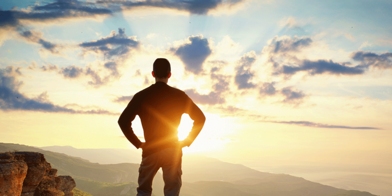 Man standing on a clifftop looking out over mountains at sunrise