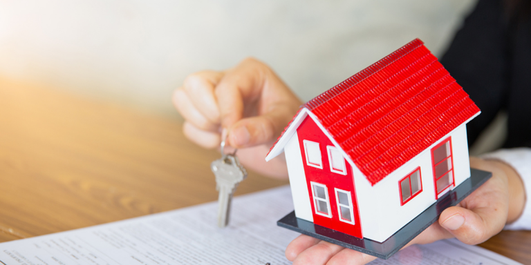 Person holding a model house and a key over a document