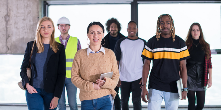 Group of people standing together indoors, one wearing a hard hat and safety vest