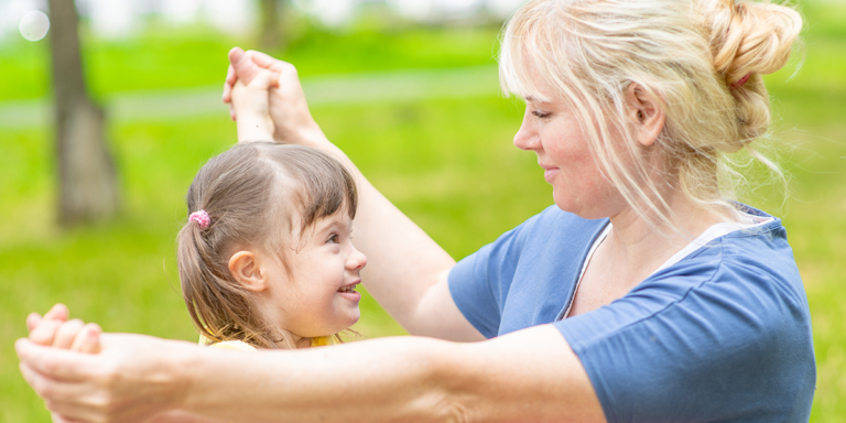 Woman holding hands with a smiling young girl outdoors