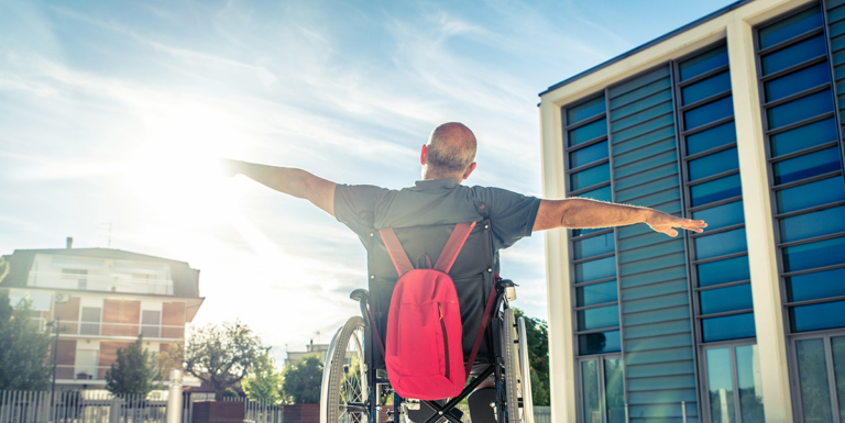 Man in a wheelchair with arms outstretched outdoors near a building