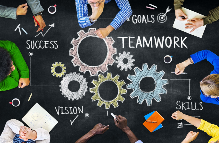 Illustration of interlocking gears labeled Teamwork surrounded by the words Success, Vision, Goals, and Skills, with people gathered around a chalkboard table