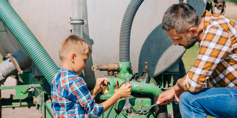 Man and boy using a wrench to work on farm machinery