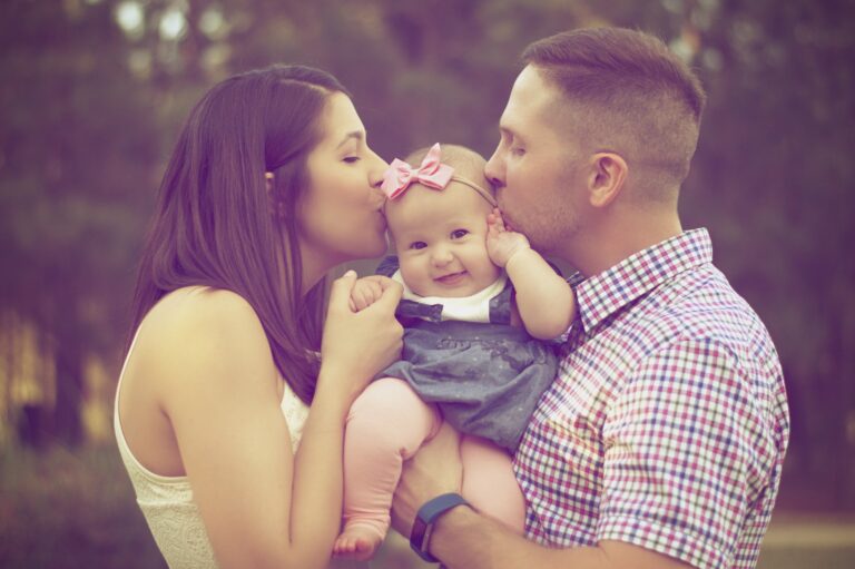 Woman and man kissing a baby held between them outdoors